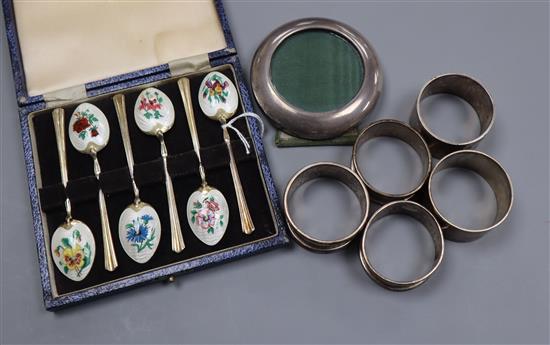 A cased set of six silver and enamel coffee spoons, five silver napkin rings and a sterling photograph frame.